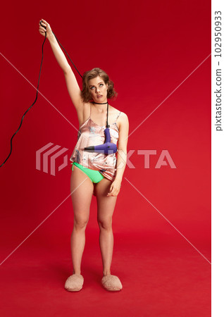 Tired stressful week. Young pretty girl wearing homewear, pajamas, holding hair dryer over head against red studio background Tired stressful week. Young pretty girl wearing homewear, pajamas, holding hair dryer over head against red studio background 102950933