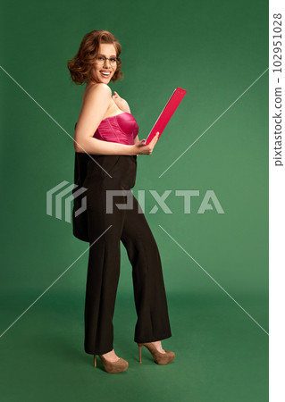 Full-length portrait of smiling, beautiful, brunette woman in formal wear with corset standing against green studio background Full-length portrait of smiling, beautiful, brunette woman in formal wear with corset standing against green studio background 102951028
