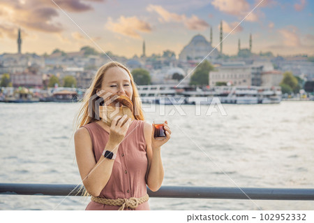 Woman in Istanbul having breakfast with Simit and a glass of Turkish tea. Glass of Turkish tea and bagel Simit against golden horn bay in Istanbul, Turkey. Turkiye Woman in Istanbul having breakfast with Simit and a glass of Turkish tea. Glass of Turkish tea and bagel Simit against golden horn bay in Istanbul, Turkey. Turkiye 102952332