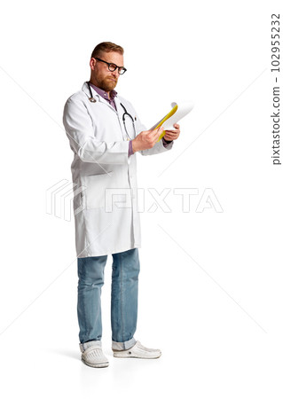 Portrait of bearded serious man, doctor in white lab coat with stethoscope reading through medical papers against white background 102955232