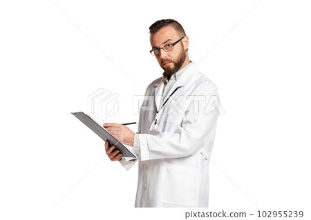 Portrait of concentrated young man, doctor in white lab coat standing, putting information in medical papers against white background Portrait of concentrated young man, doctor in white lab coat standing, putting information in medical papers against white background 102955239