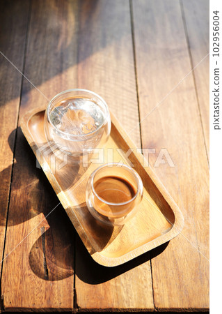 Hot coffee and glass of ice on wooden tray under sunlight 102956004