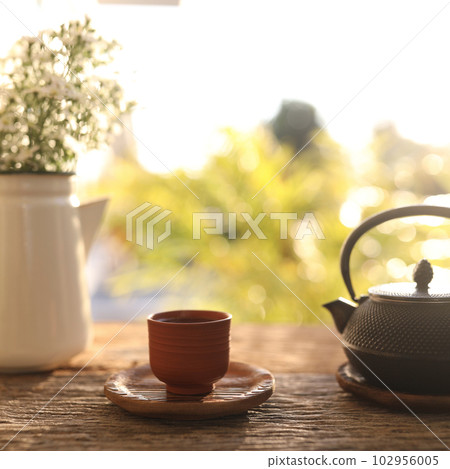 Tea cup and black metal tea pot and flowers on wooden table Tea cup and black metal tea pot and flowers on wooden table 102956005