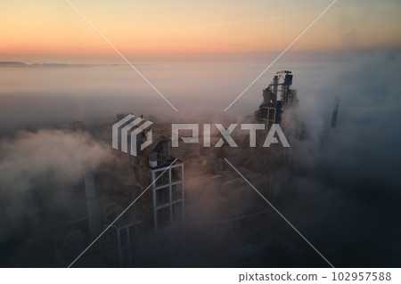 Aerial view of cement factory with high concrete plant structure and tower crane at industrial manufacturing site on foggy evening. Production and global industry concept. Aerial view of cement factory with high concrete plant structure and tower crane at industrial manufacturing site on foggy evening. Production and global industry concept. 102957588