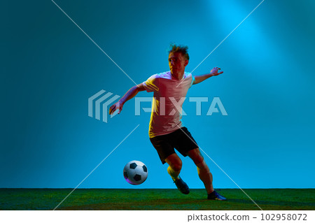 One energetic guy, sportsman, soccer player wearing black and white uniform training on football field in neon light. Concept of action, energy, sport 102958072