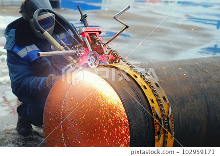 Welder in mask cuts large-diameter pipe with autogenous gun and sparks fly. Device for cutting metal Welder in mask cuts large-diameter pipe with autogenous gun and sparks fly. Device for cutting metal 102959171