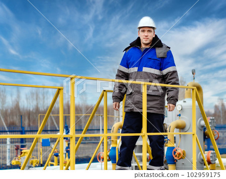 Portrait of worker in white helmet and winter pea jacket at industrial gas facility. Middle-aged Portrait of worker in white helmet and winter pea jacket at industrial gas facility. Middle-aged 102959175