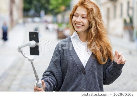 Young redheaded beautiful woman walking and using her mobile phone Young redheaded beautiful woman walking and using her mobile phone 102960102
