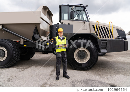 Man worker with tablet computer stands next to mining truck. Man worker with tablet computer stands next to mining truck. 102964564