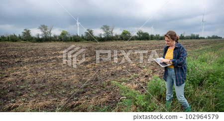 Farmer with laptop on the field. Wind turbines on a horizon. Smart sustainable farming and agriculture digitalization. 102964579