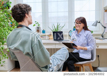 Mature female counselor, educational center social worker talking to young teenage guy Mature female counselor, educational center social worker talking to young teenage guy 102964802