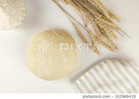 Raw dough, flour and ears of wheat on white background, top view. Home baking concept. Raw dough, flour and ears of wheat on white background, top view. Home baking concept. 102966418