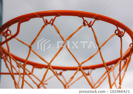 Basketball hoop on backyard against blue sky. Sports recreation and healthy living in nature. Orange red rope net on a street. Equipment on a playground. Training tools on stadium. Play outdoors. Basketball hoop on backyard against blue sky. Sports recreation and healthy living in nature. Orange red rope net on a street. Equipment on a playground. Training tools on stadium. Play outdoors. 102966421