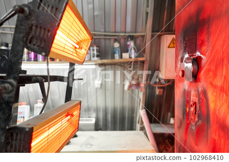 The coloring test is dried under a warm lamp. Garage painting car service. Repairing car body work after the accident by working sanding primer before painting. The coloring test is dried under a warm lamp. Garage painting car service. Repairing car body work after the accident by working sanding primer before painting. 102968410