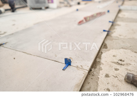 Tiler work. Repair of the dining room in the house, place for kitchen, floor covering change. Empty interior for design, gray concrete wall. 102968476