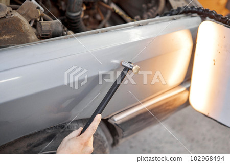 A car service worker knocks with a hammer. Removing dents on the car. PDR technology. Car body repair without painting. A car service worker knocks with a hammer. Removing dents on the car. PDR technology. Car body repair without painting. 102968494