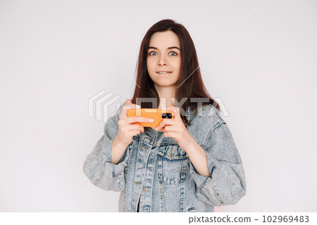 Indecisive and Insecure: Young Woman in Denim Jacket Playing Smartphone Game, Isolated on Gray Indecisive and Insecure: Young Woman in Denim Jacket Playing Smartphone Game, Isolated on Gray 102969483
