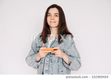 Portrait of a young woman in a casual denim jacket with a smartphone playing a game, isolated 102969484