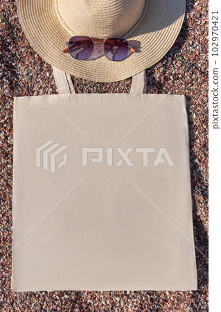 Summer beach accessories. Mockup of linen eco bag, straw hat and sunglasses on pebble beach. Summer beach accessories. Mockup of linen eco bag, straw hat and sunglasses on pebble beach. 102970421