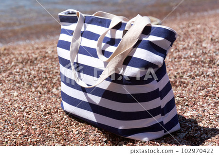 Beach striped bag on pebble beach near the sea. Summer background. Beach striped bag on pebble beach near the sea. Summer background. 102970422