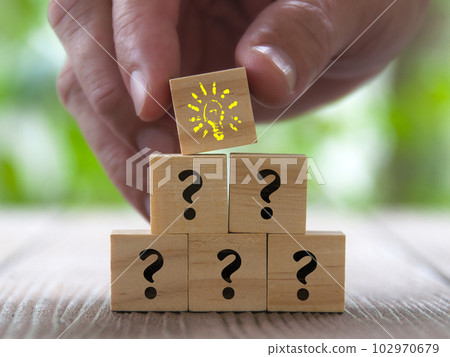 Hand placing wooden cube with yellow color light bulb on top of other cubes with question mark. Idea concept Hand placing wooden cube with yellow color light bulb on top of other cubes with question mark. Idea concept 102970679