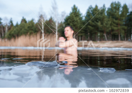 Man going ice swimming into a frozen lake during winter. Man standing between the ice pieces and meditating. 102972839