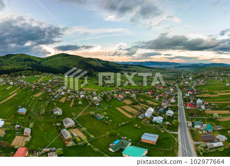 Aerial landscape view of village houses and distant green cultivated agricultural fields with growing crops on bright summer day Aerial landscape view of village houses and distant green cultivated agricultural fields with growing crops on bright summer day 102977664