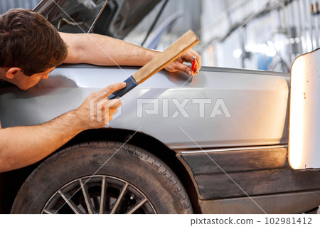 A car service worker knocks with a hammer. Removing dents on the car. PDR technology. Car body repair without painting. 102981412