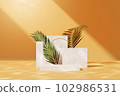 Front view of smooth yellow wall background with light in the center. Geometric platforms with marble material arranged with palm leaves. Space for advertising cosmetics product.  102986531