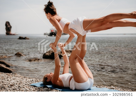 Woman sea yoga. Two Happy women meditating in yoga pose on the beach, ocean and rock mountains. Motivation and inspirational fit and exercising. Healthy lifestyle outdoors in nature, fitness concept. 102986561