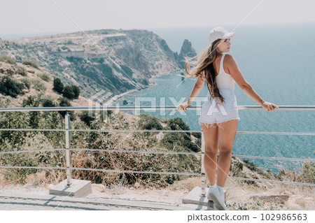 Woman summer travel sea. Happy tourist enjoy taking picture outdoors for memories. Woman traveler posing over sea bay surrounded by volcanic mountains, sharing travel adventure journey 102986563