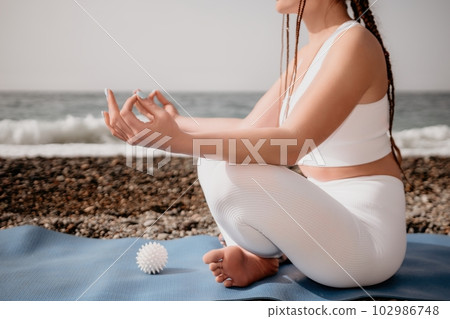 Close up Yoga Hand Gesture of Woman Doing an Outdoor meditation. Blurred sea background. Woman on yoga mat in beach meditation, mental health training or mind wellness by ocean, sea. Selective focus 102986748