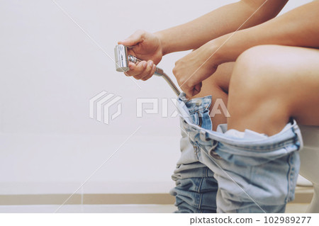 Cropped image of man sitting excrete on toilet. His jeans is hanging on his legs in toilet. Cropped image of man sitting excrete on toilet. His jeans is hanging on his legs in toilet. 102989277