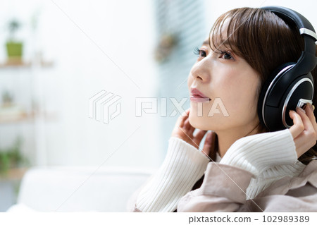 A woman sitting on a sofa and listening to music 102989389