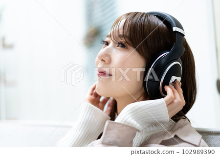 A woman sitting on a sofa and listening to music A woman sitting on a sofa and listening to music 102989390