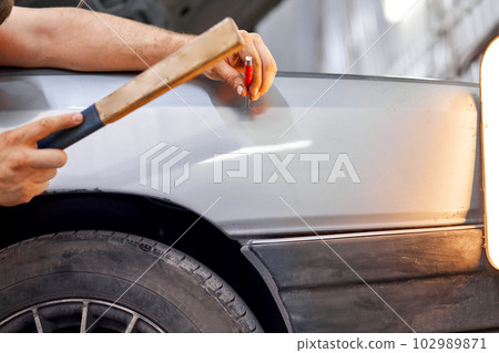 A car service worker knocks with a hammer. Removing dents on the car. PDR technology. Car body repair without painting. 102989871