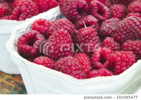 Close-up of a container of fresh, red, ripe raspberries at an open-air food market 102995477