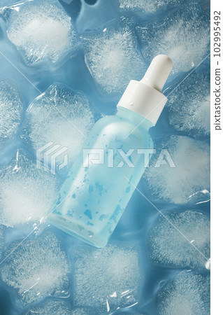 Bottle of blue serum on ice cubes and water background. Bottle of blue serum on ice cubes and water background. 102995492