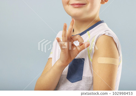Vaccinated kid boy is gesturing okay and showing arm with adhesive bandage 102998453