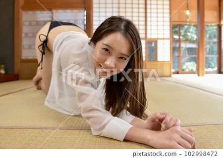 A smiling young woman in a black bikini swimsuit posing in a Japanese-style room A smiling young woman in a black bikini swimsuit posing in a Japanese-style room 102998472
