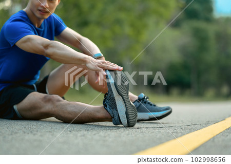 Shot of active sportsman in fitness clothes stretching leg, preparing for morning workout in the public park 102998656