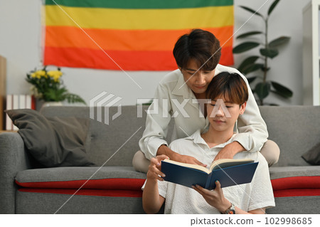 Image of passionate gay couple sitting in living room and reading book. LGBT, love and lifestyle concept 102998685