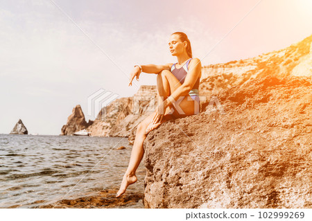 Woman travel summer sea. A happy tourist in a blue bikini enjoying the scenic view of the sea and volcanic mountains while taking pictures to capture the memories of her travel adventure. Woman travel summer sea. A happy tourist in a blue bikini enjoying the scenic view of the sea and volcanic mountains while taking pictures to capture the memories of her travel adventure. 102999269