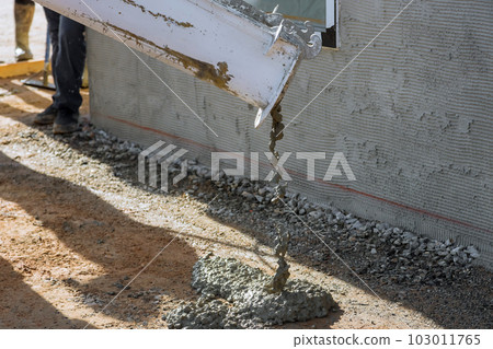 As concrete mixing truck pours concrete for pavement surrounding newly constructed home on construction site 103011765