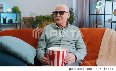 Grandfather man on sofa eating popcorn and watching interesting TV serial, sport game online at home Grandfather man on sofa eating popcorn and watching interesting TV serial, sport game online at home 103013444