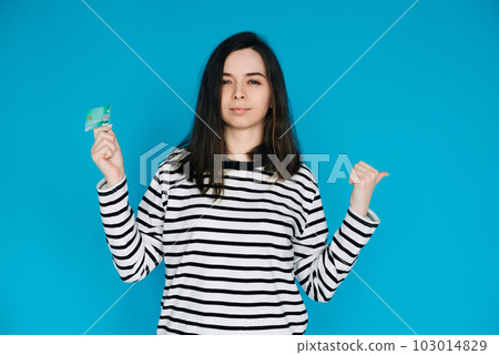 Woman Holding Credit Card, Pointing with Thumb in Empty Space - Female Expressing Confidence and Woman Holding Credit Card, Pointing with Thumb in Empty Space - Female Expressing Confidence and 103014829
