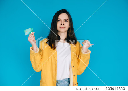 Happy Woman Pointing Thumb at Empty Space with Credit Card - Positive and Attractive Female Happy Woman Pointing Thumb at Empty Space with Credit Card - Positive and Attractive Female 103014830