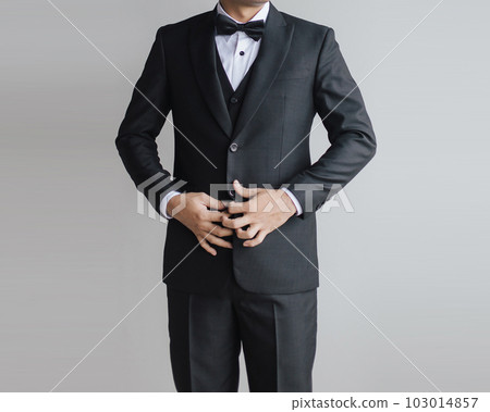 Detail half body close up a man black suit with vest inside with bow tie and white shirt opening the suit or fixing it by holding the suit button. Detail half body close up a man black suit with vest inside with bow tie and white shirt opening the suit or fixing it by holding the suit button. 103014857