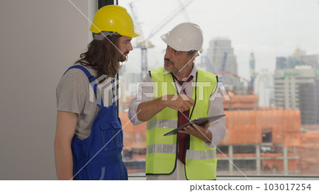 Senior engineer contractor holding tablet assigning work to male electrician 103017254