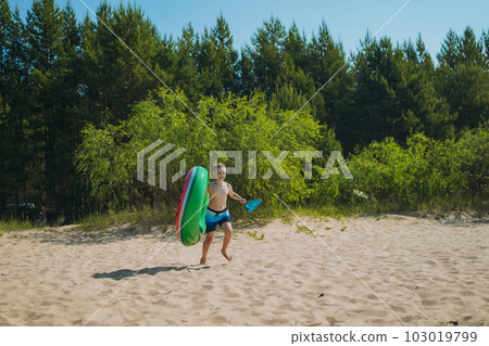 cute caucasian boy carrying rubber ring and butterfly net running into water with laughter. Vacation on sea side. Happy childhood. Image with selective focus. cute caucasian boy carrying rubber ring and butterfly net running into water with laughter. Vacation on sea side. Happy childhood. Image with selective focus. 103019799